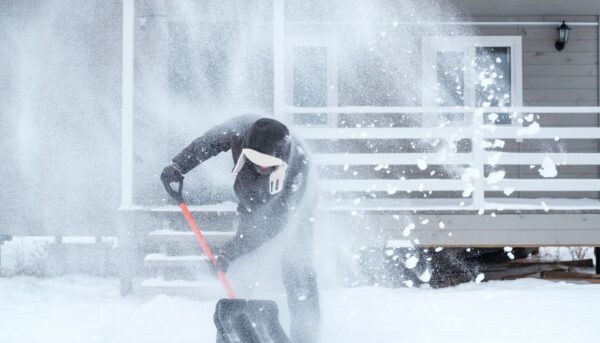 clearing snow near the house after a heavy snowfall. a man shovels snow near a wooden house.